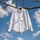 White floral shirt hanging on a tree branch with a blue sky background