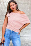Woman wearing a pink off-shoulder top and blue jeans against a gray wall.