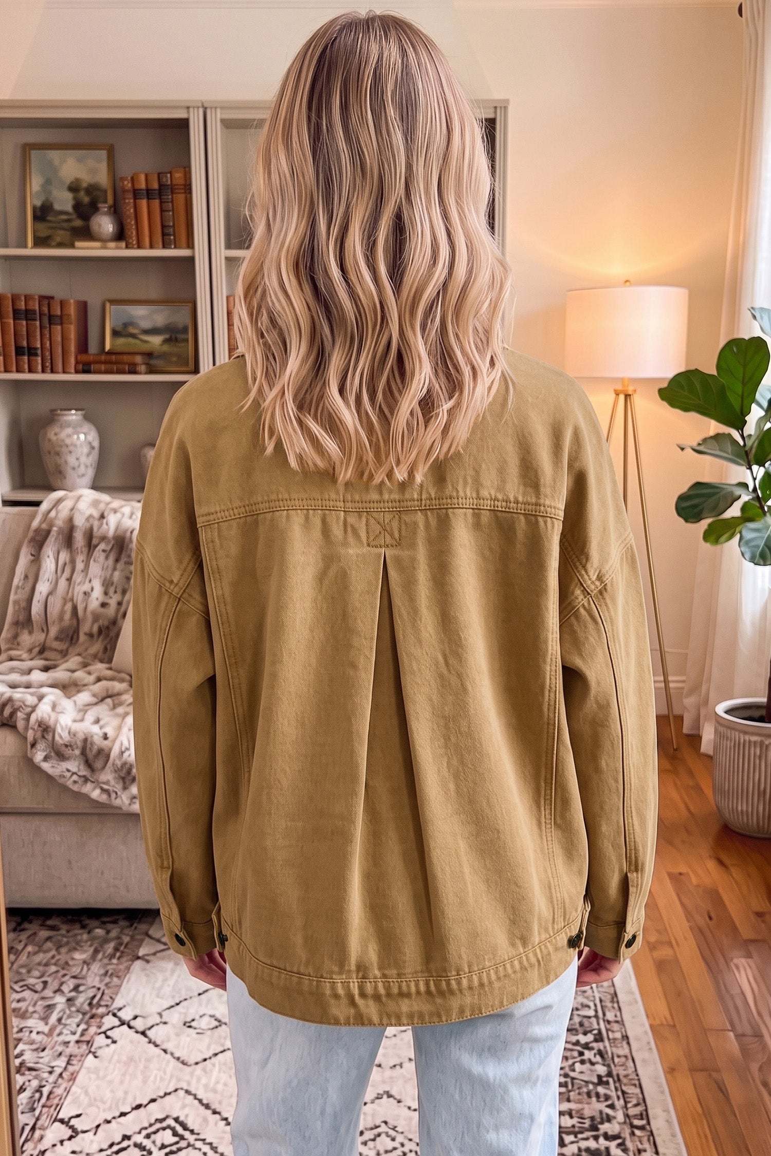 Woman viewed from behind wearing tan canvas utility jacket with back pleat detail and light blue jeans.