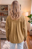 Woman viewed from behind wearing tan canvas utility jacket with back pleat detail and light blue jeans.