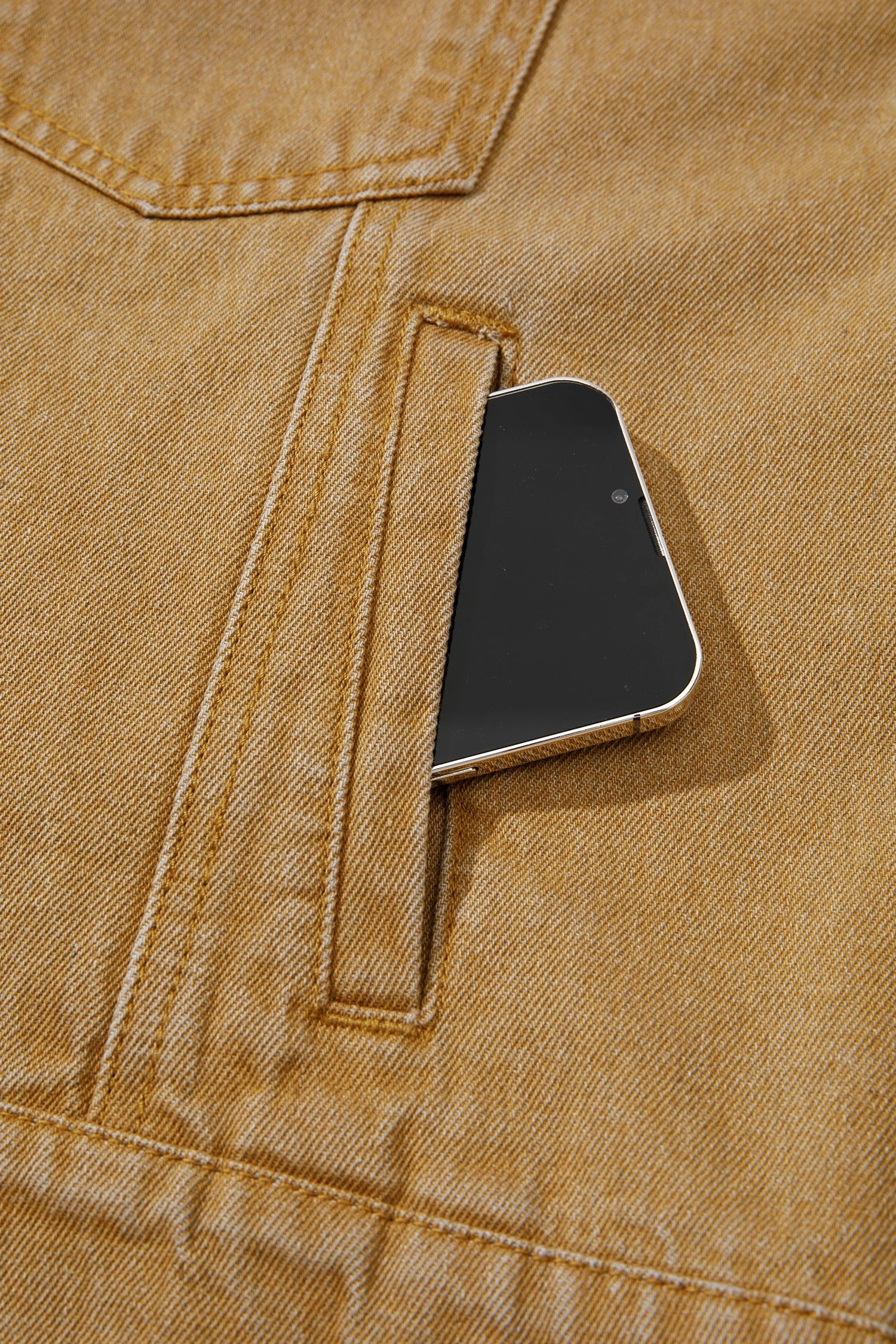 Close-up of a black smartphone partially tucked into a side pocket of a tan denim jacket.