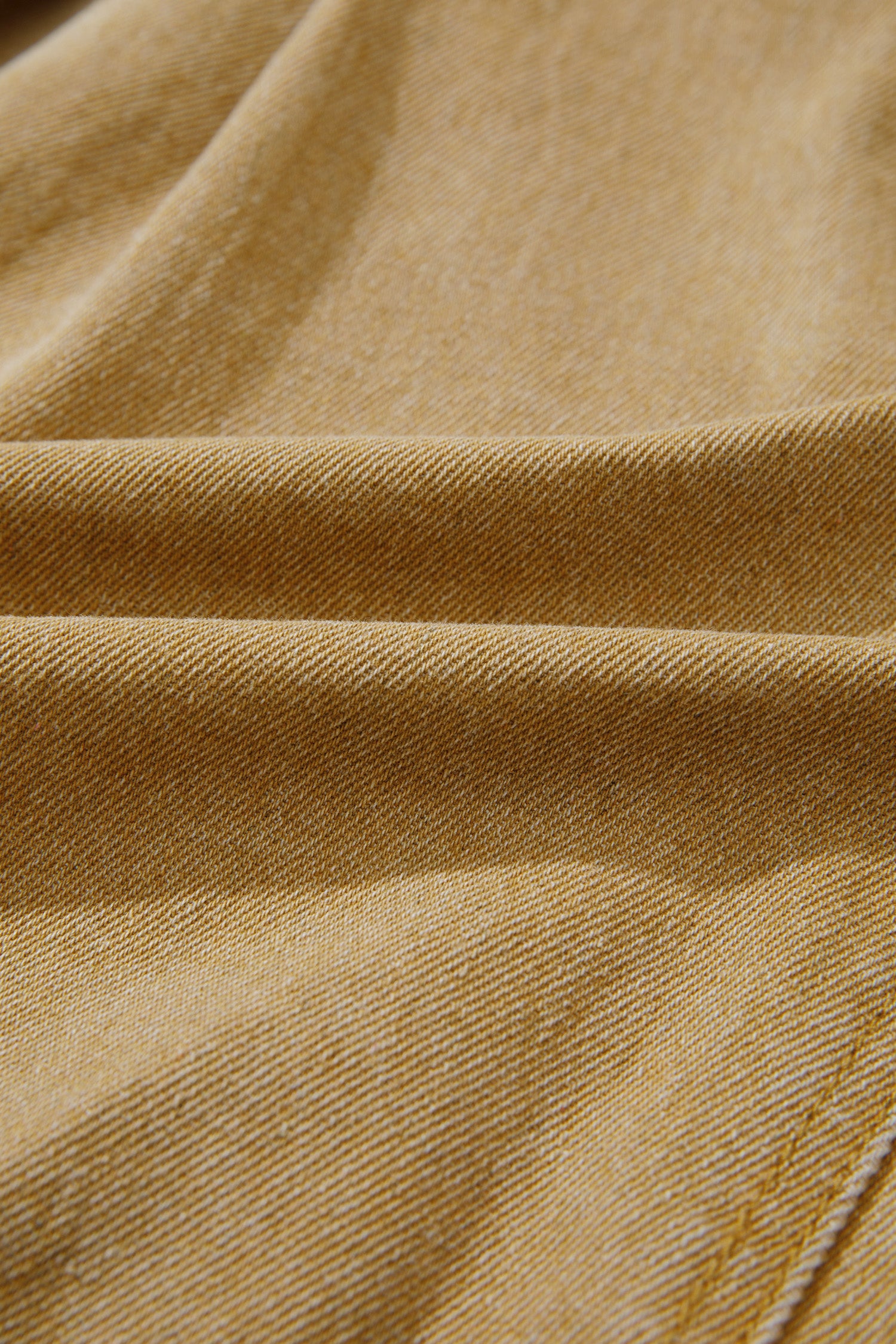 A close-up of draped tan fabric with a fine twill texture and subtle diagonal stitching.