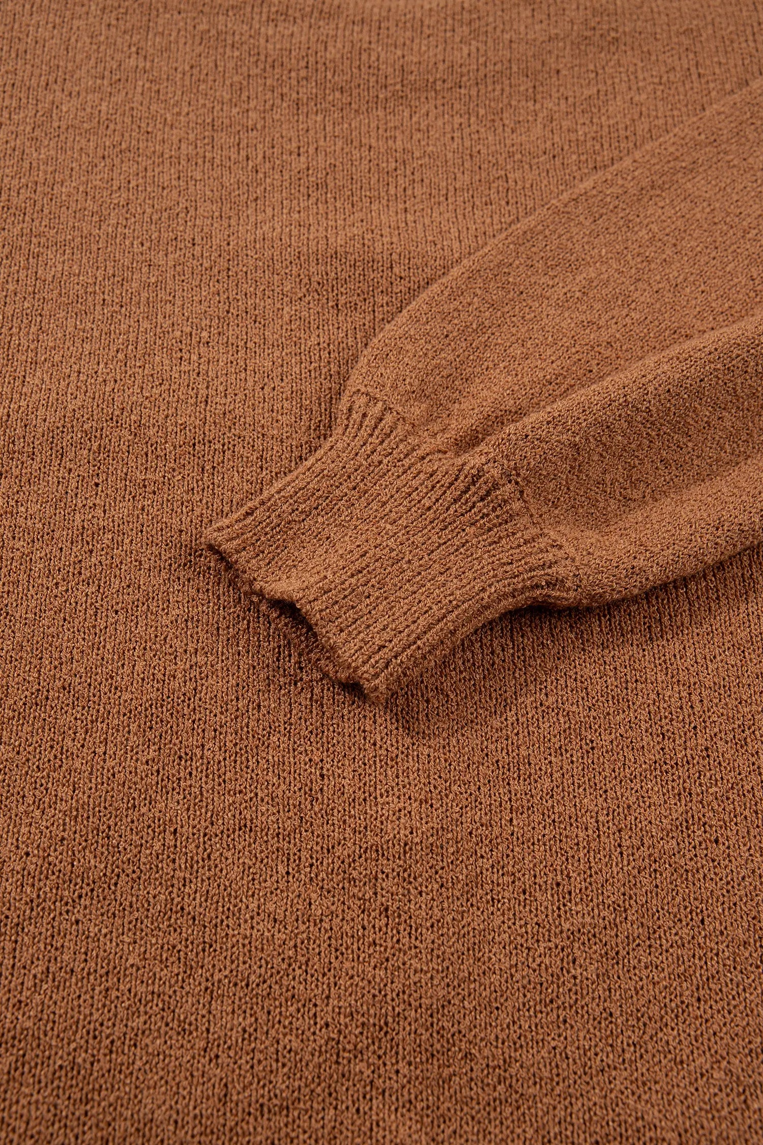 Close-up of a brown knit sweater showing the ribbed cuff of a sleeve, highlighting the fine knit texture.