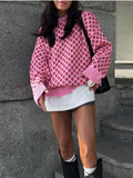 Person wearing a pink patterned sweater and white skirt standing against a stone wall.