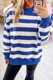 A woman takes a mirror selfie wearing a blue and white horizontally striped mock-neck sweatshirt and black pants in a retail store setting.