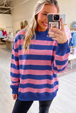 A woman taking a mirror selfie in a clothing store, wearing a long-sleeve crewneck sweatshirt with horizontal pink and navy blue stripes.