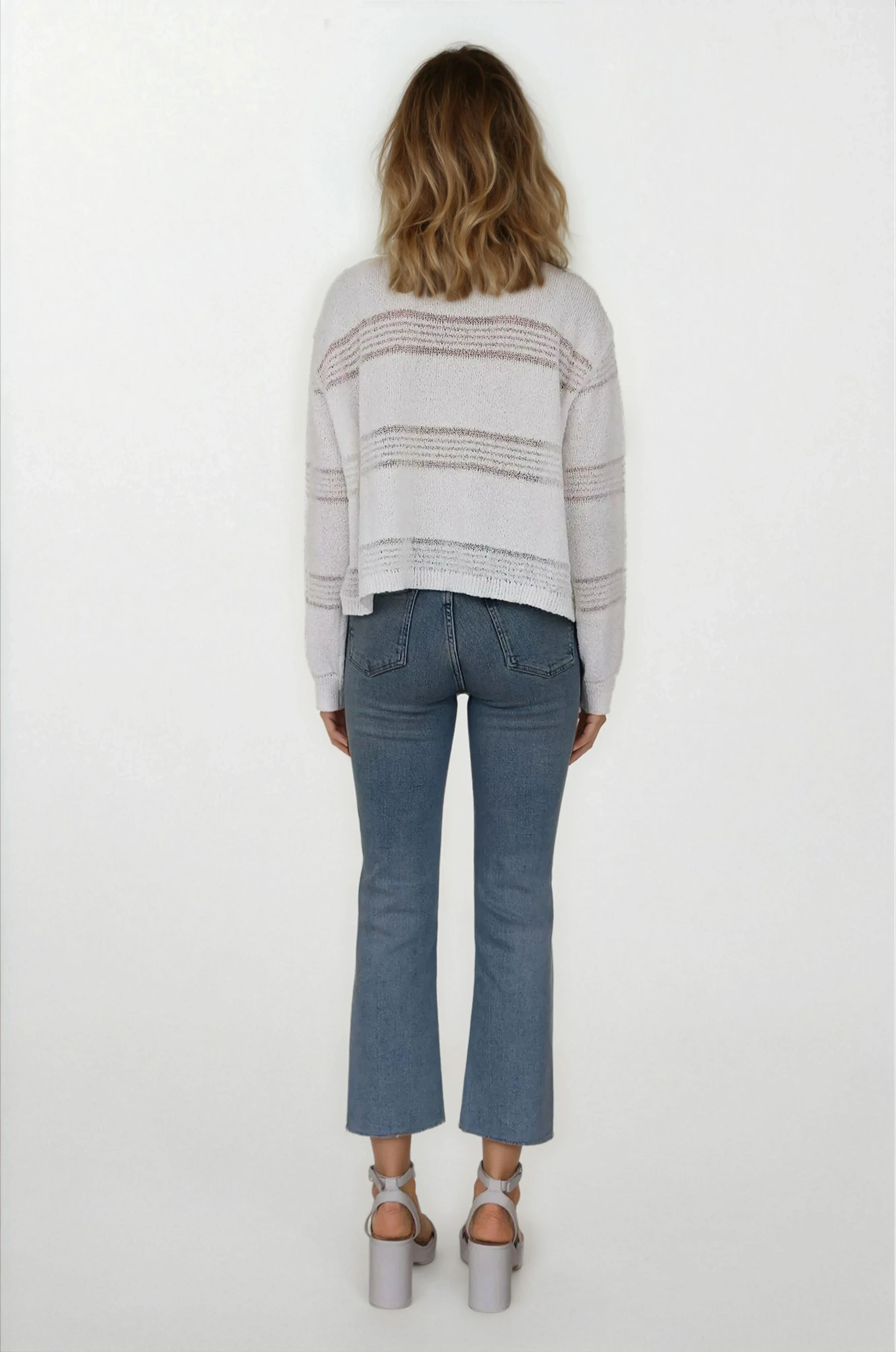 Person wearing a striped sweater and blue jeans on a white background