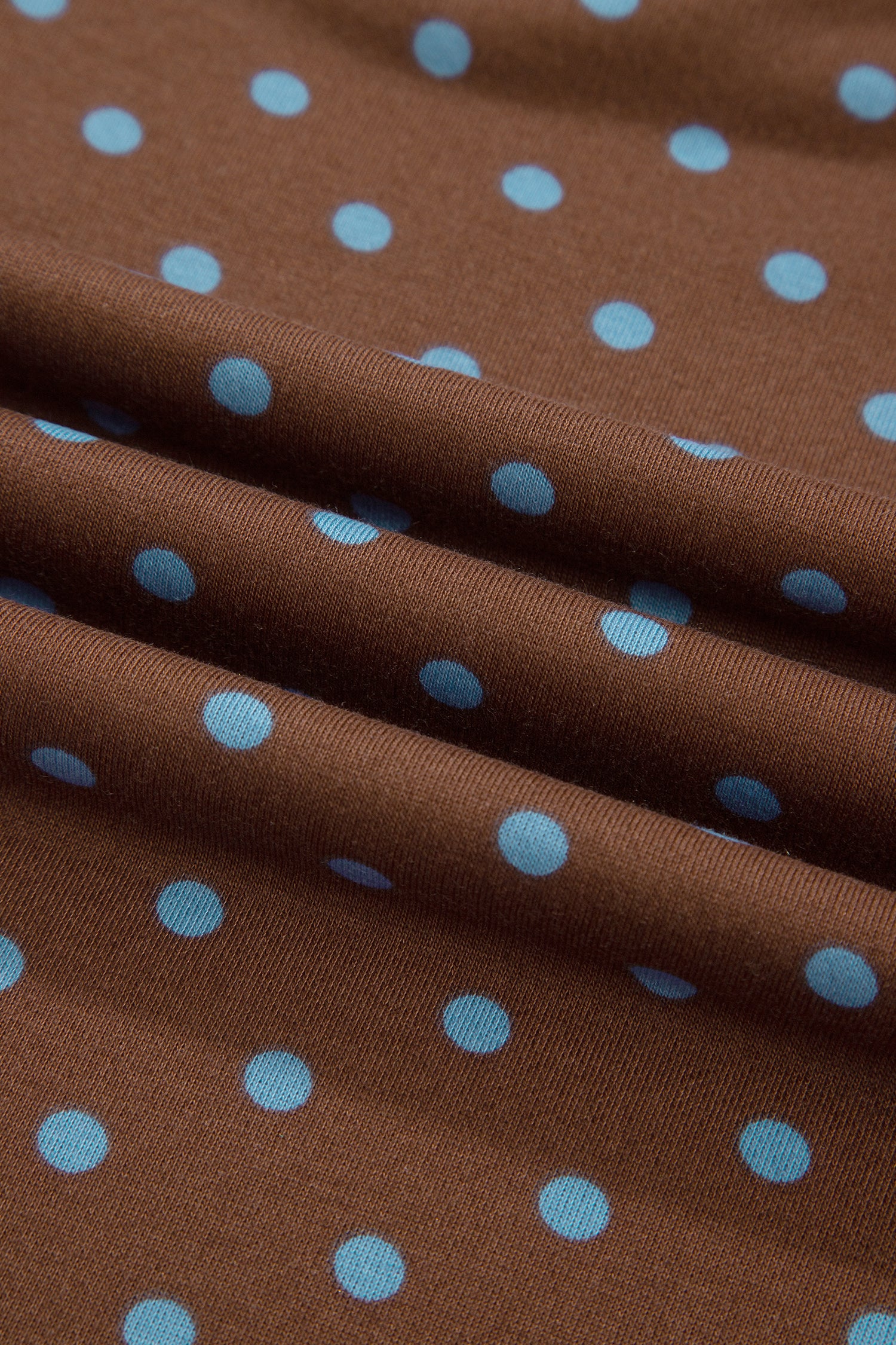 Brown knit fabric with a light blue polka dot pattern, shown in soft folds.