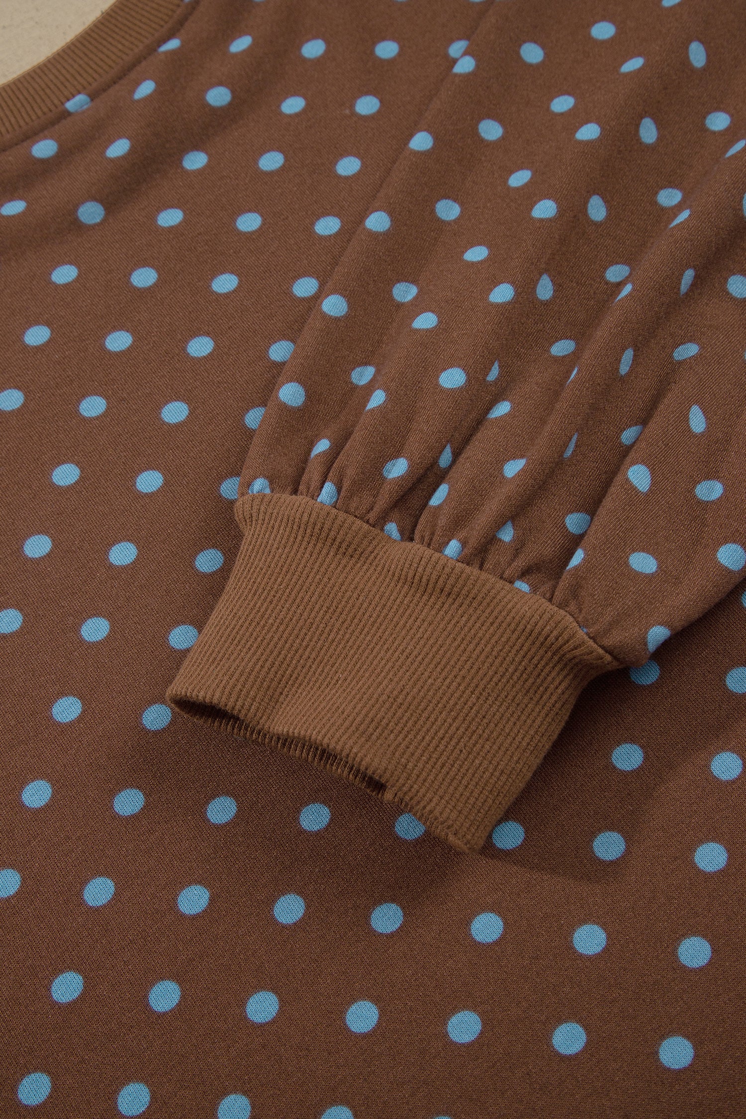 Close-up of a brown knit garment with light blue polka dots and a ribbed cuff.