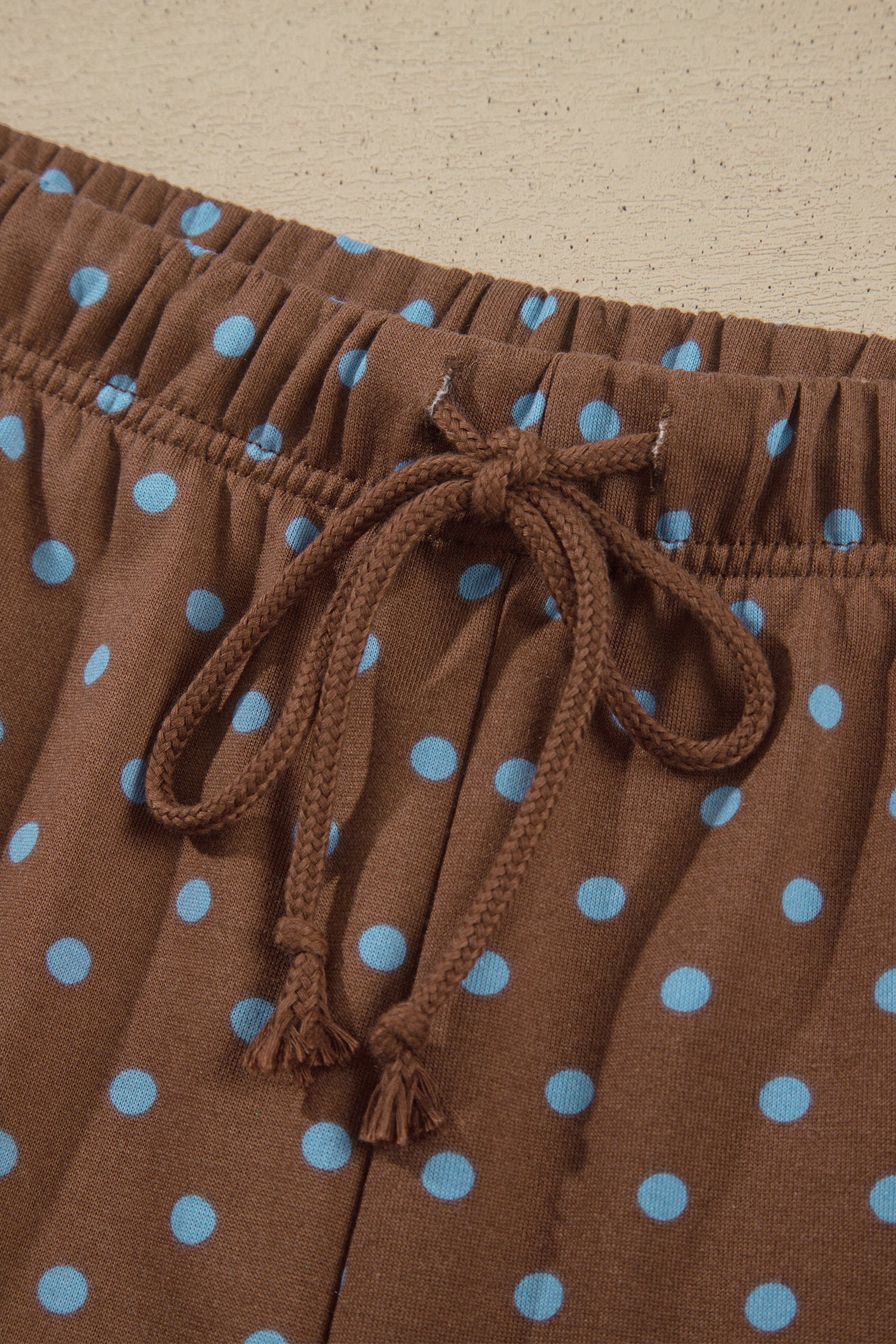 Close-up of brown drawstring shorts with light blue polka dots, showing the elastic waistband and drawstring tied in a bow.