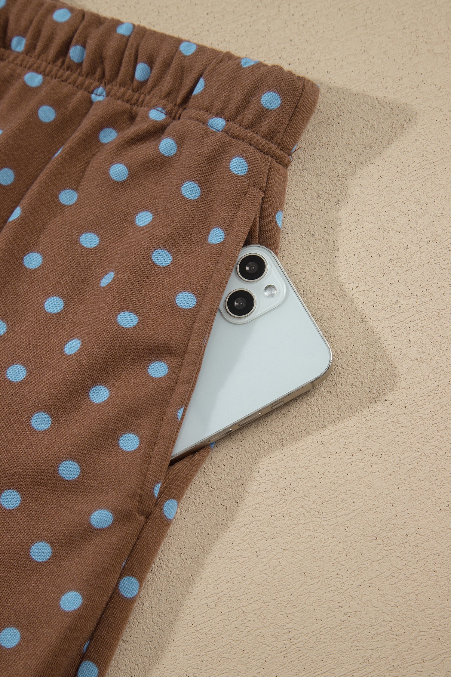 Brown polka-dot pants with light blue dots and a side pocket holding a white smartphone.