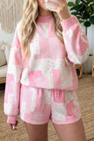 A woman wearing a pink and white patchwork pajama set with a long-sleeve sweatshirt and matching shorts, taking a mirror selfie in a cozy indoor setting.