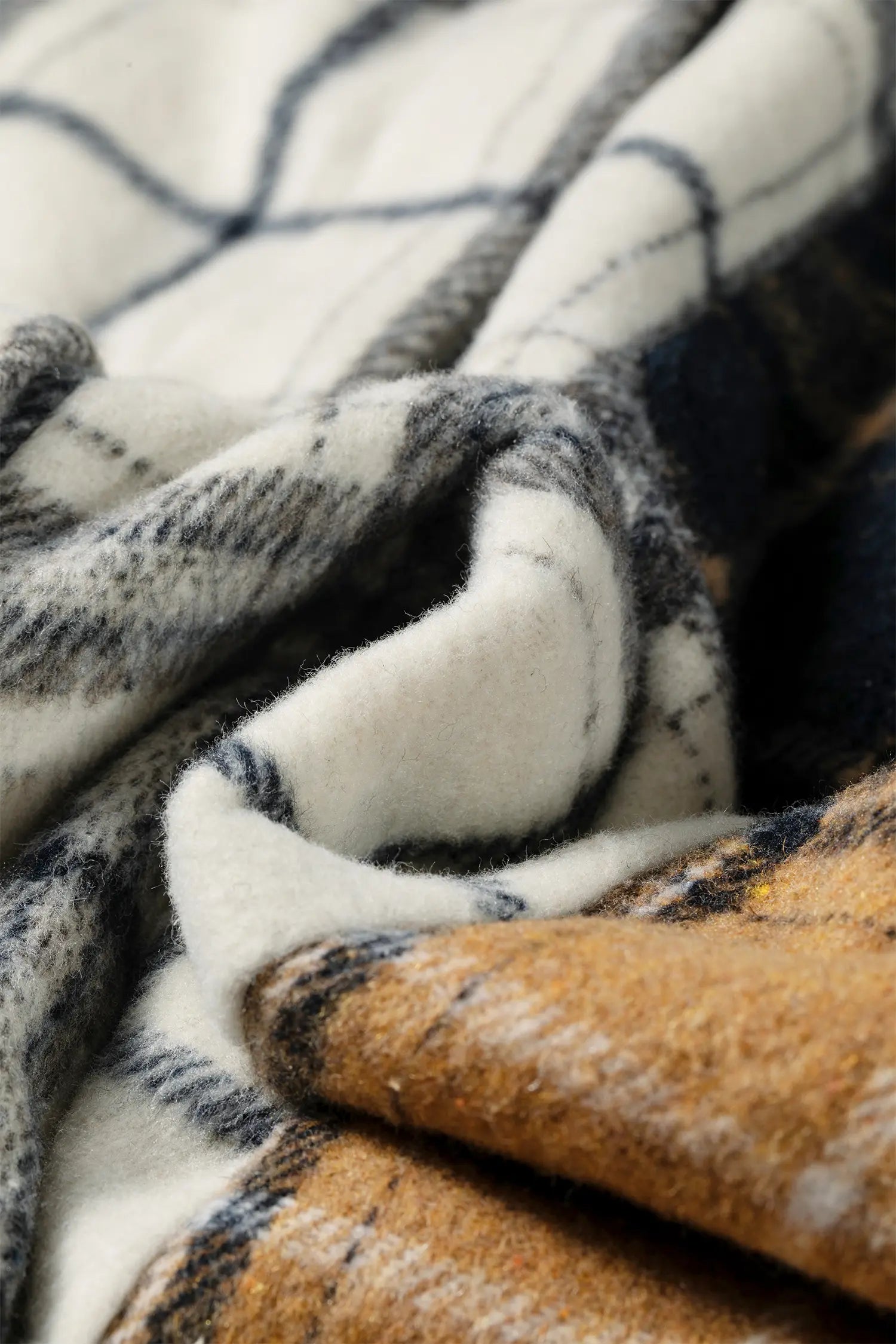 Close-up of a soft woven blanket or throw with a plaid pattern, showing cream, navy, gray, and tan sections with a plush texture.