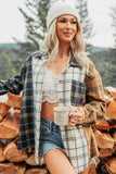 A woman outdoors wearing a beige knit beanie, a cream lace camisole, denim shorts, and an oversized navy, beige, and brown plaid flannel shirt, holding a white mug with 'The Peace' written on it.