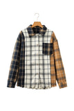 A patchwork plaid button-up shirt jacket hanging on a wooden hanger against a plain white background. The shirt features a central white plaid panel with black lines, navy blue plaid sleeves, and a tan plaid side panel.