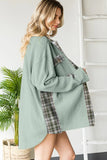 Woman wearing a green ribbed sweater over a plaid shirt with a white background