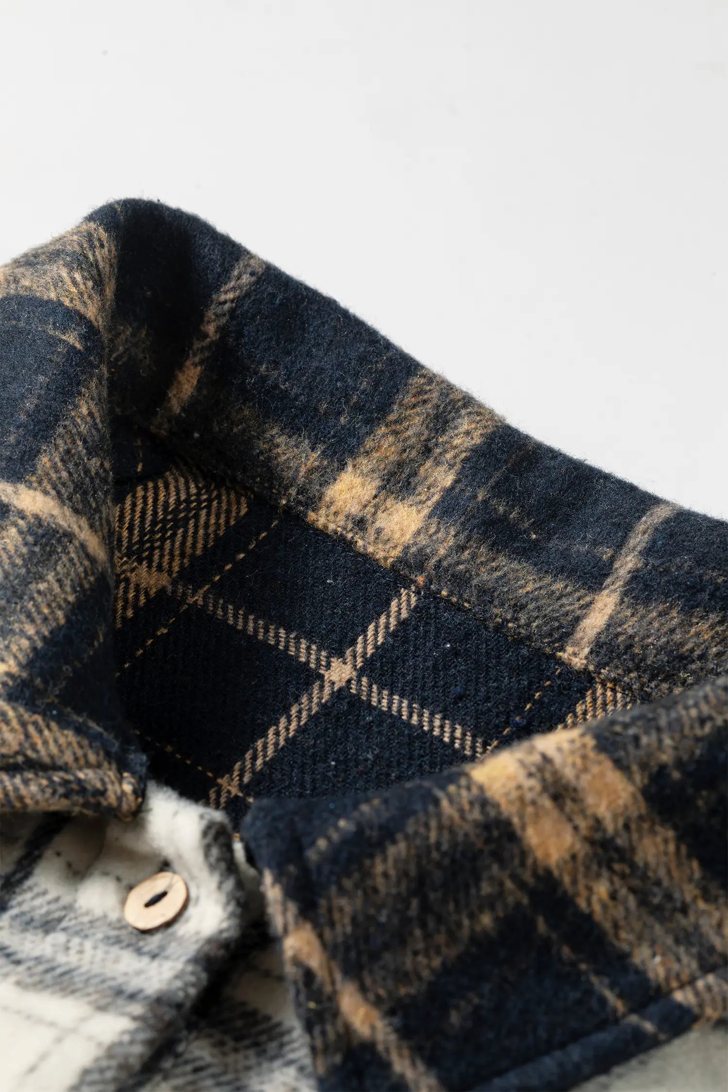 Close-up of a plaid button-up shirt collar in dark navy and tan tones, with a light-colored plaid shirt underneath partially visible.