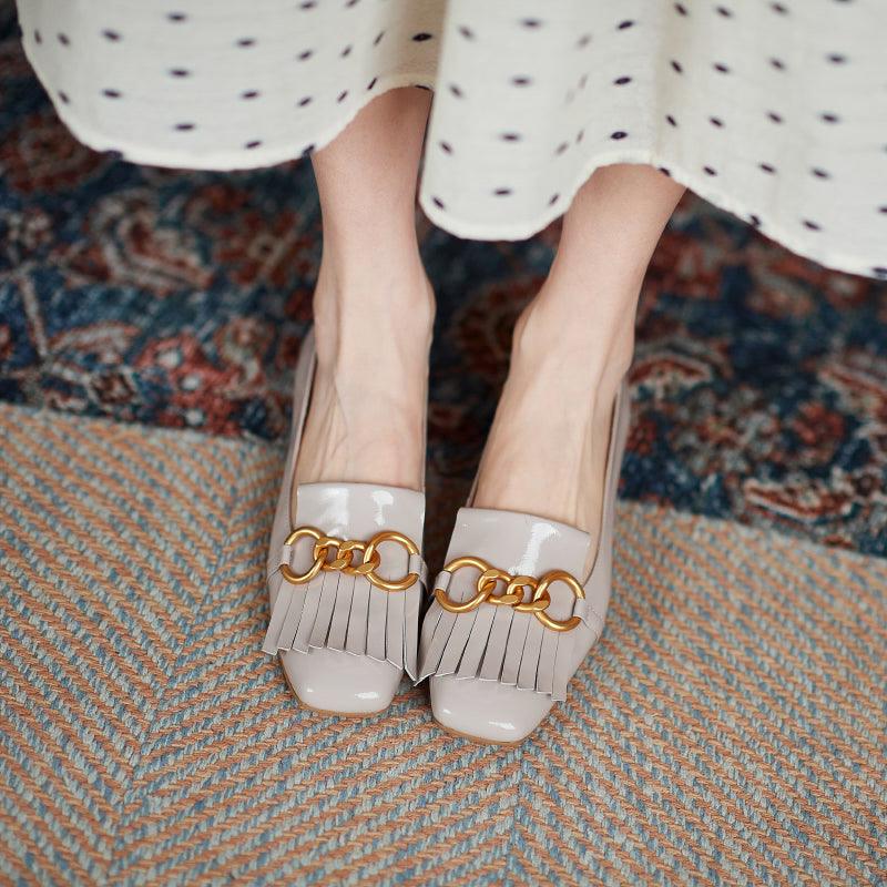 White shoes with gold chain detail worn by a person on a patterned rug.