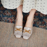 White shoes with gold chain detail worn by a person on a patterned rug.