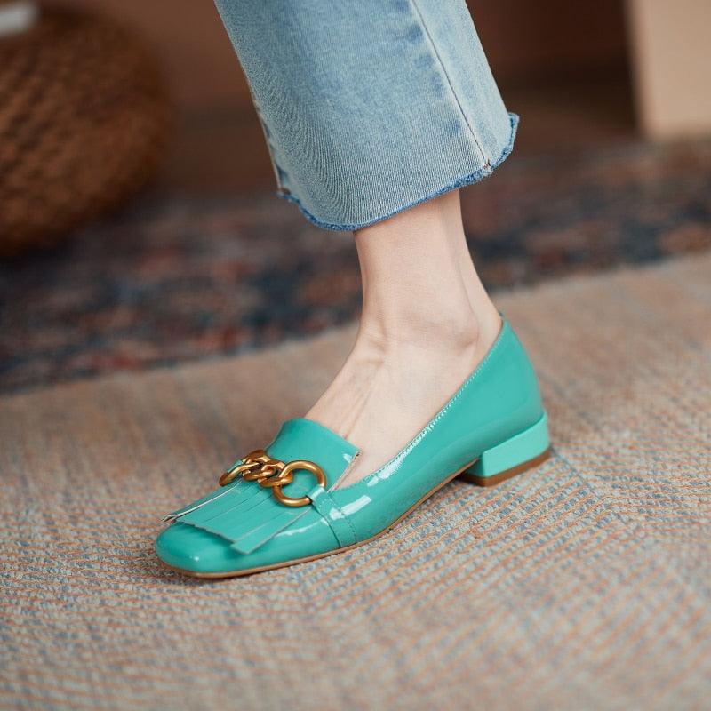 Teal loafers with gold chain detail worn with light blue jeans on a textured surface.
