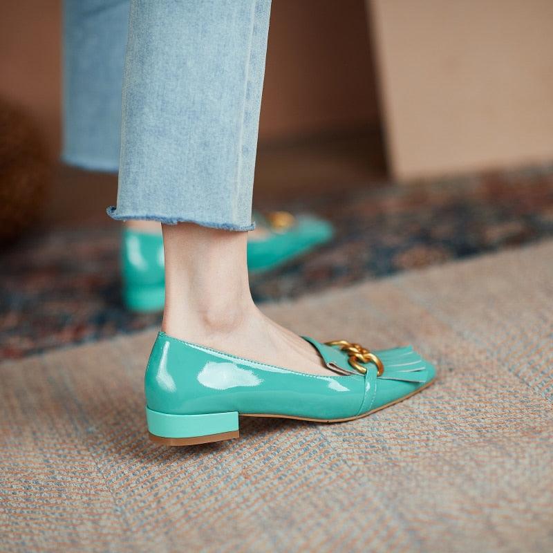 Teal patent leather shoes with gold accents worn with light blue jeans on a patterned carpet.