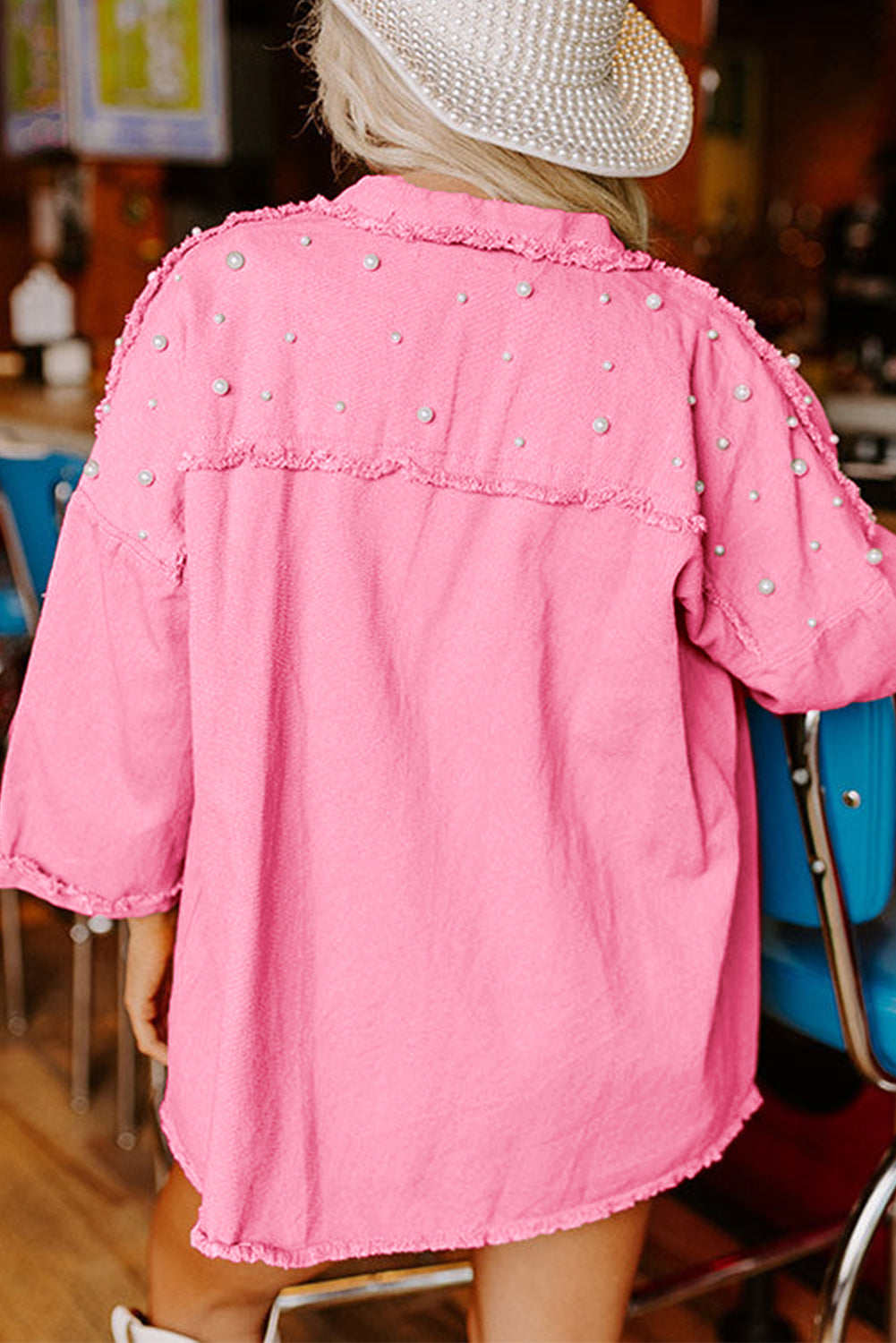 Person wearing a pink jacket with pearl embellishments in an indoor setting