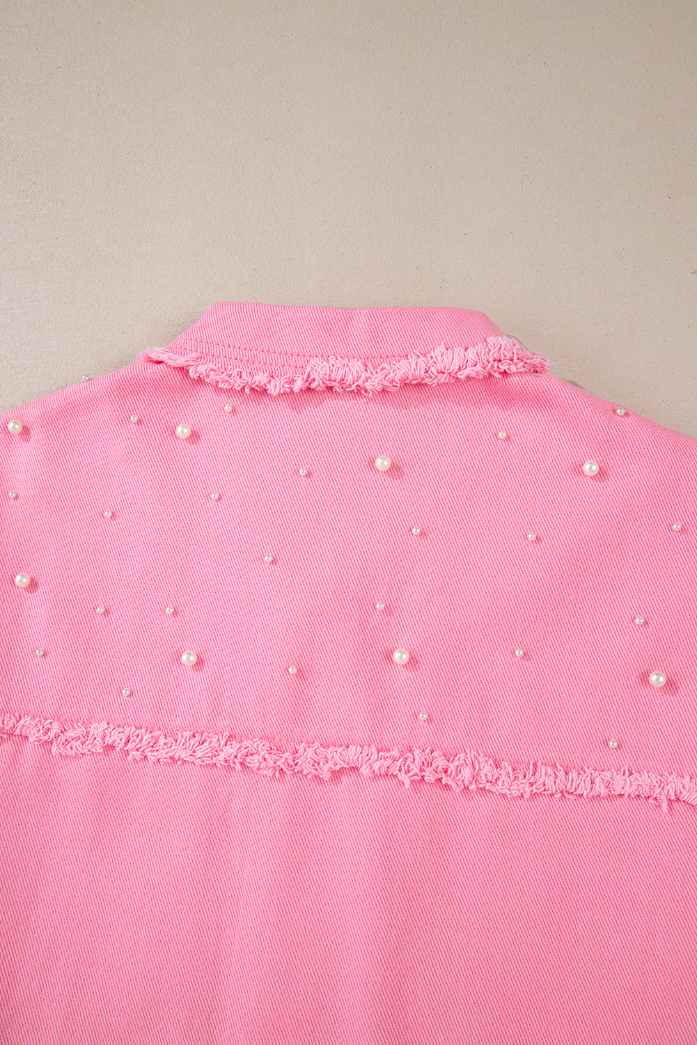 Pink garment with pearl embellishments on a beige background