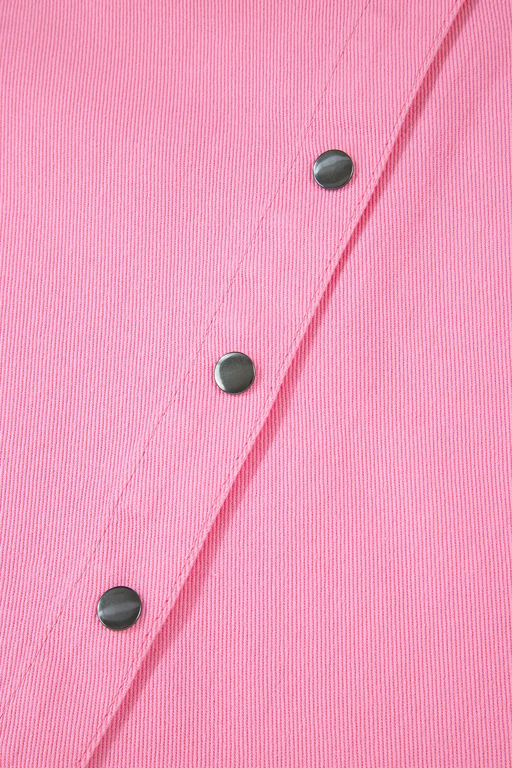 Close-up of a pink textured fabric with three dark metallic snap buttons aligned diagonally.