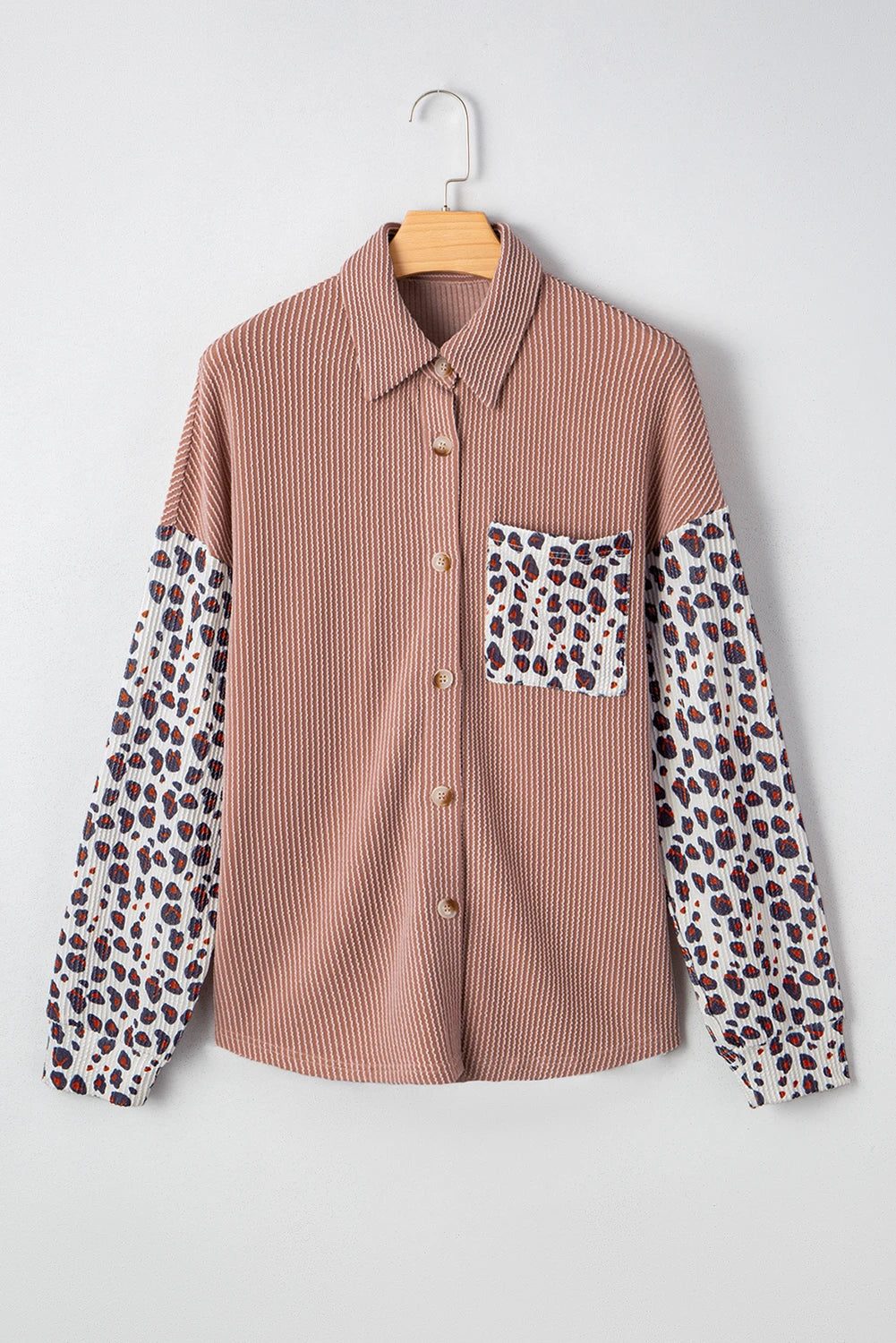 Brown shirt with leopard print sleeves and pocket on a hanger against a white background.
