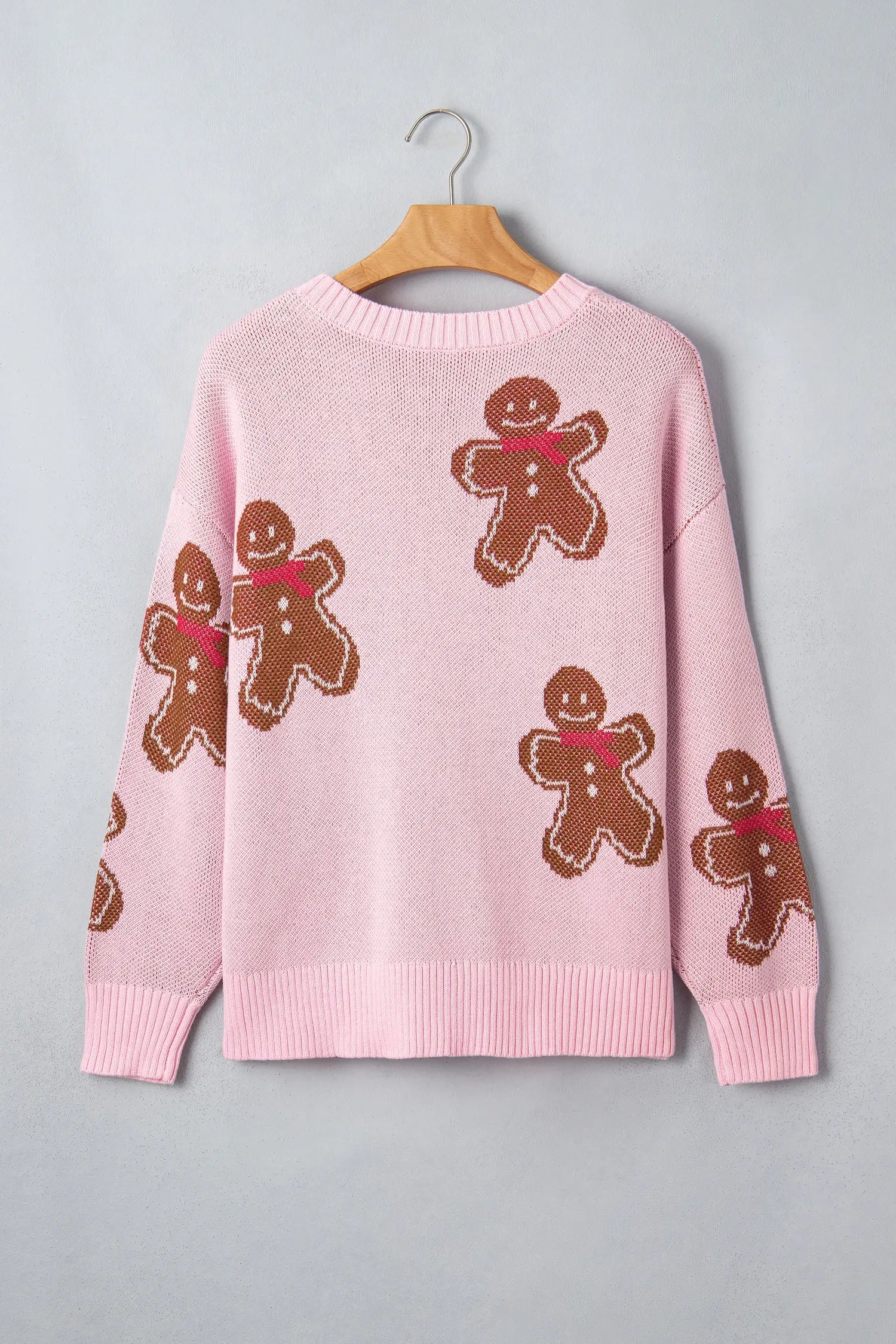 Pink knit sweater with brown gingerbread men motifs and red scarves on hanger against light gray.