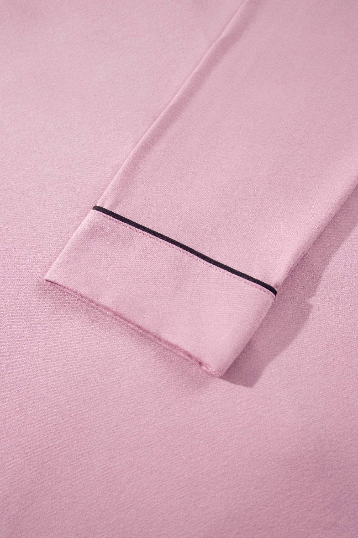 A close-up of a light pink fabric garment, likely pajama pants or a lounge set, showing a folded cuff with a thin black piping trim against a matching pink background.