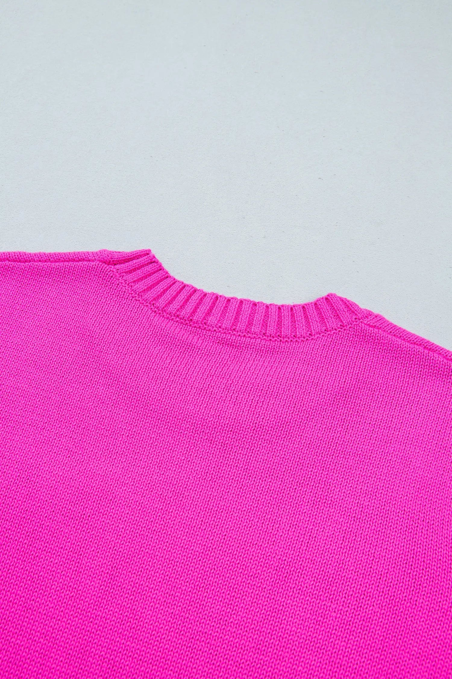 Close-up of bright pink knit sweater with ribbed crew neck collar.