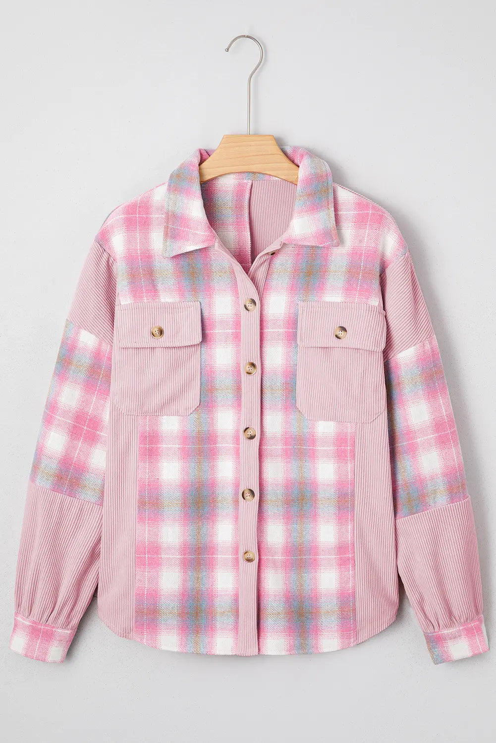 A pink plaid button-up shirt jacket with textured corduroy sleeves and chest pockets, hanging on a wooden hanger against a light gray background.