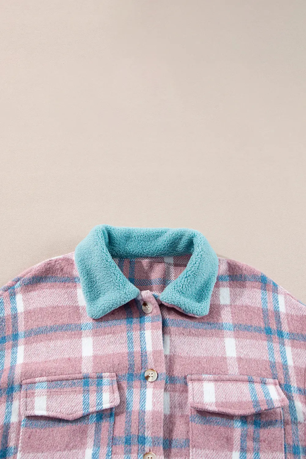 A close-up of a plaid flannel shirt with a soft teal fleece collar, featuring pink, white, and blue plaid pattern and silver buttons.