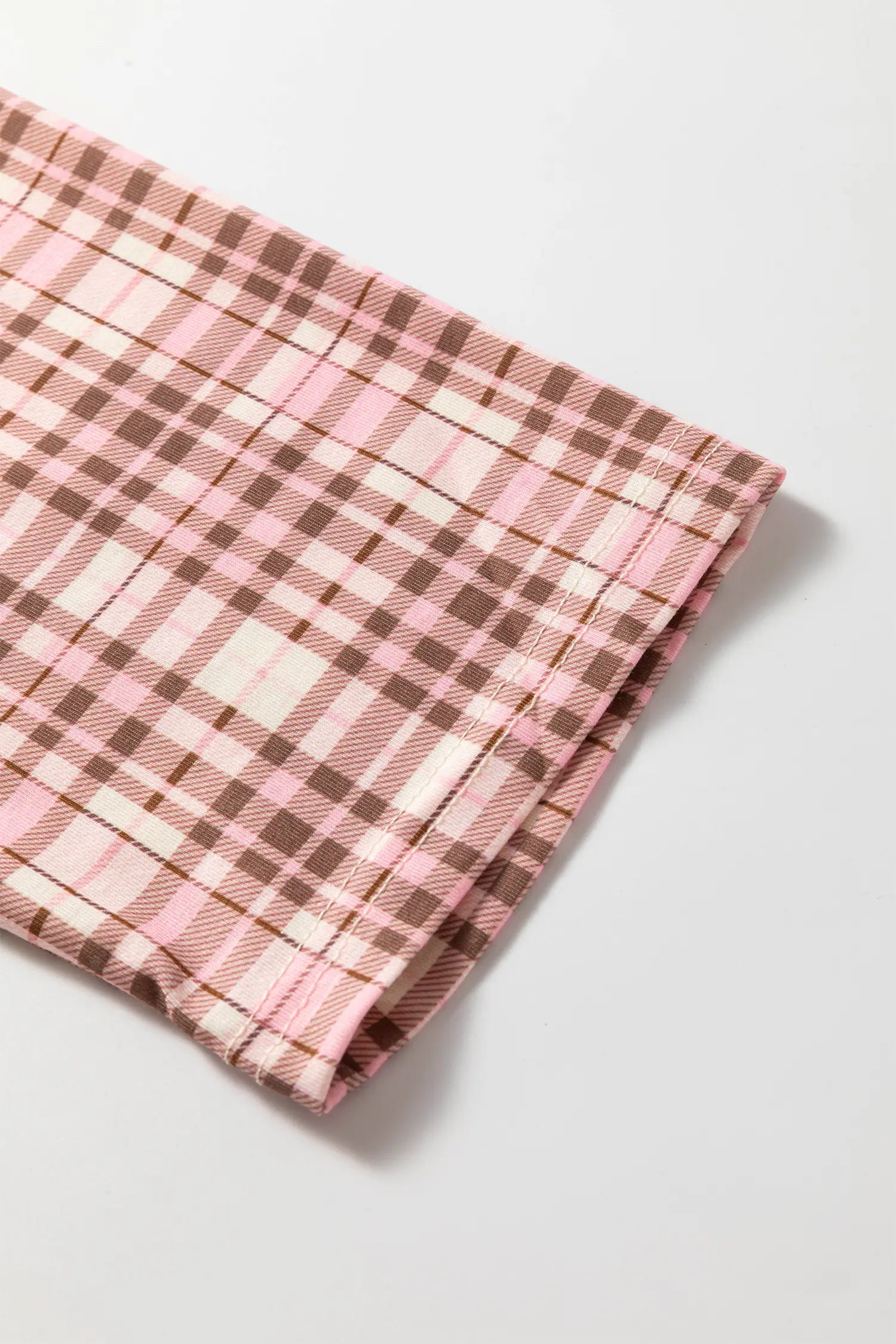 Folded pink, brown, and cream plaid fabric on a gray background.