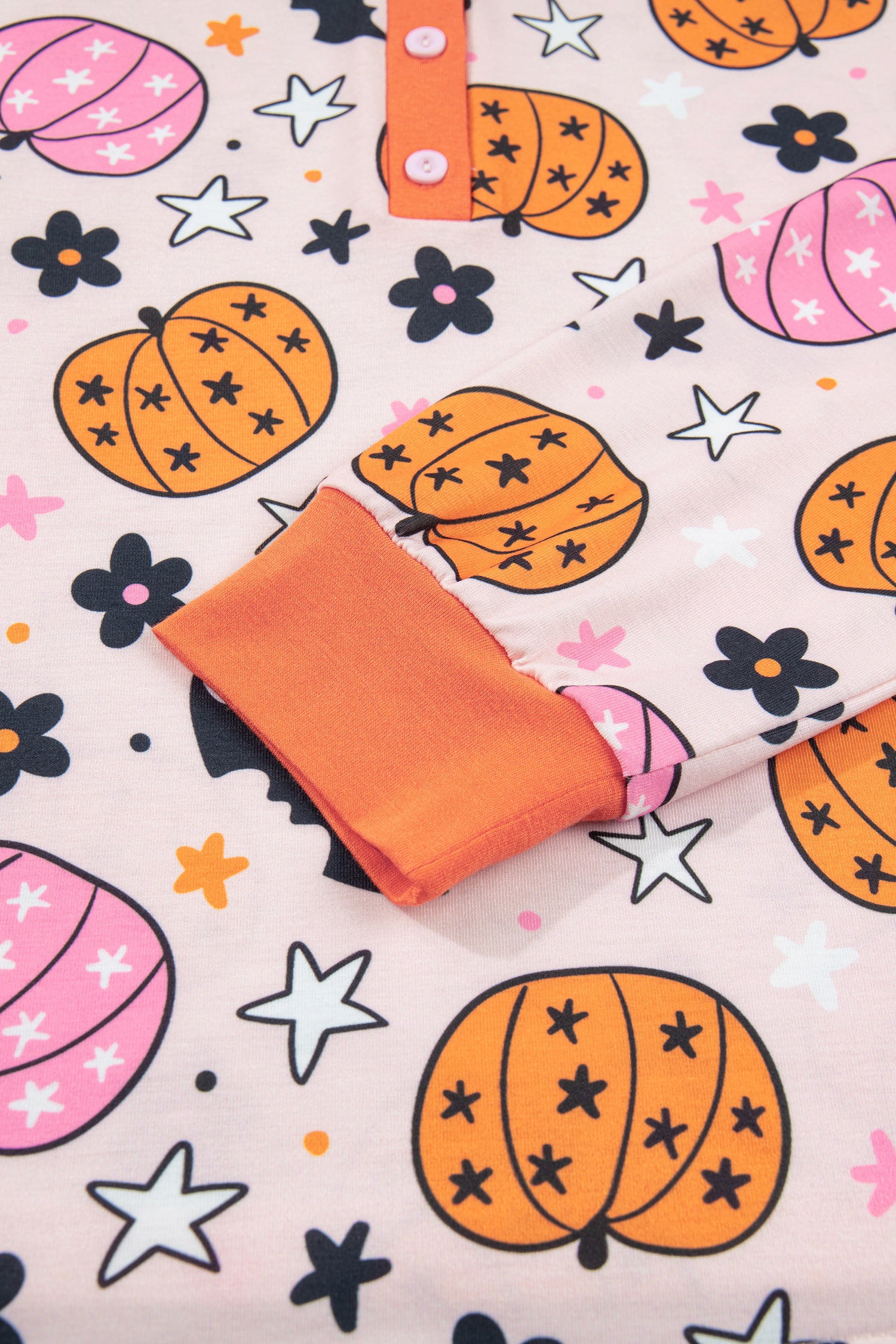 Close-up of pale pink Halloween fabric with pumpkins, pink motifs, flowers, stars, and orange trim.