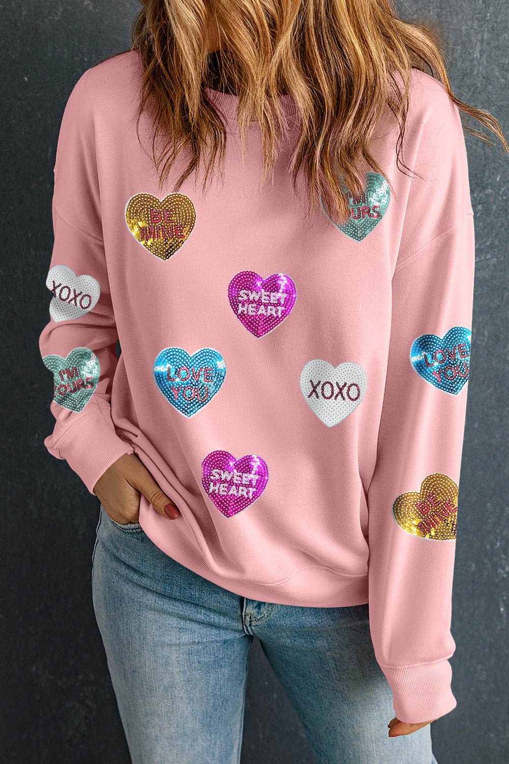 Person wearing a pink sweatshirt with colorful heart patterns on a dark background