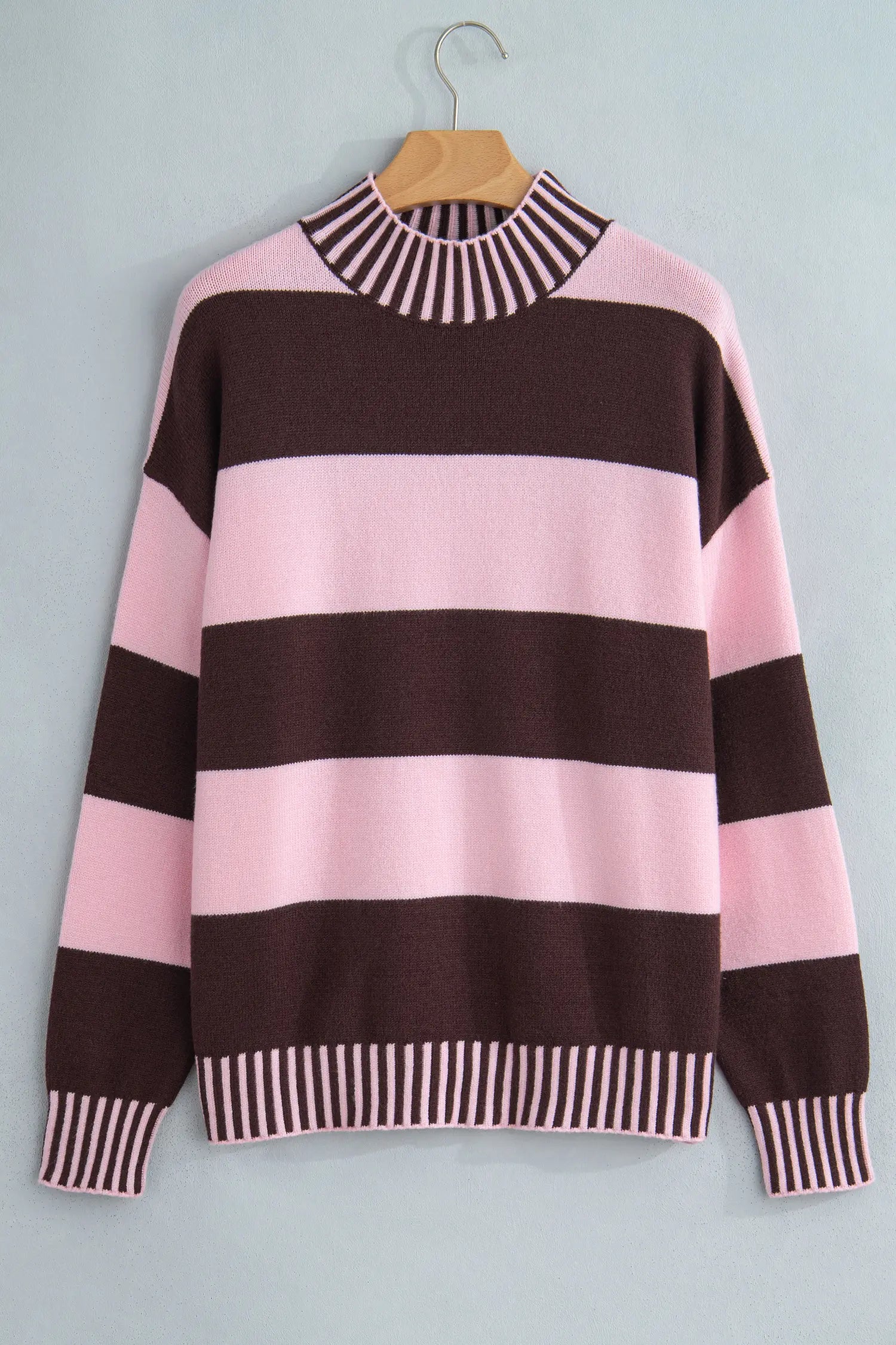 A pink and dark brown striped knit sweater with striped ribbed trim, hanging on a wooden hanger against a light gray background.