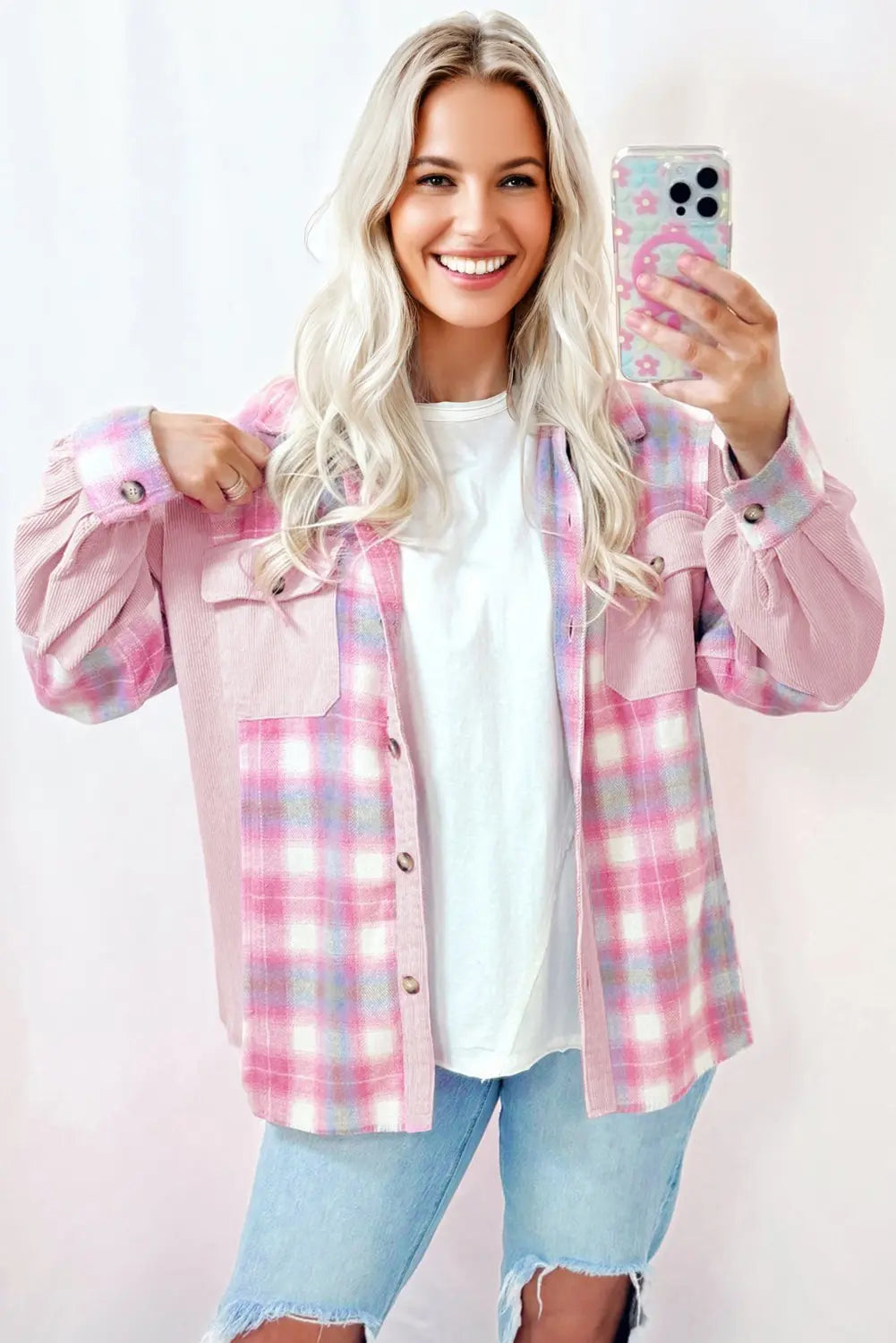 Woman wearing a pink plaid shirt taking a selfie on a light pink background