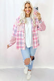 Woman wearing a pink plaid shirt over a white top and ripped jeans, standing against a white background.