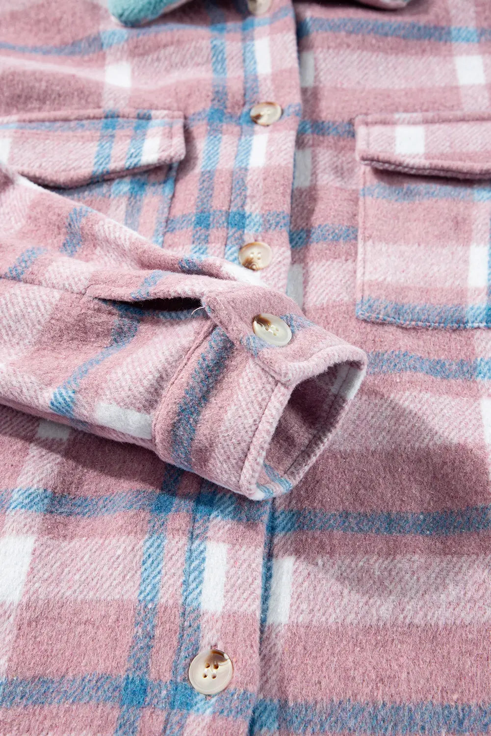 Close-up of a pink plaid flannel shirt jacket with blue and white stripes, showing the fabric texture, button details, and pocket flaps.