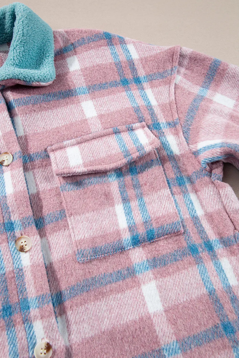 Close-up of a pink and blue plaid shirt with a pocket and buttons.