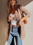Woman wearing a plaid jacket, white top, and blue jeans with a brown bag against a neutral background