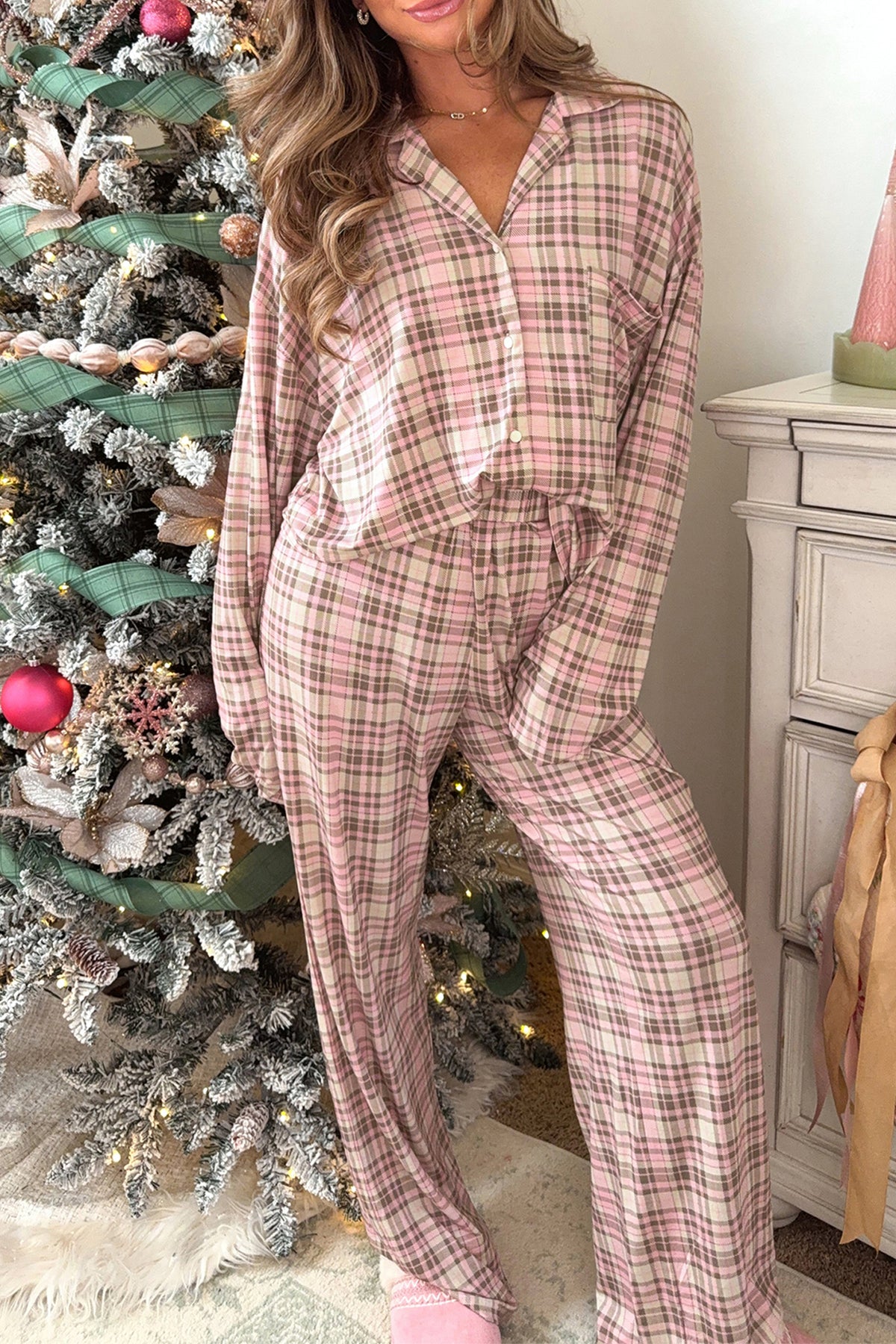 Woman wearing pink and beige plaid Christmas pajamas by a tree.