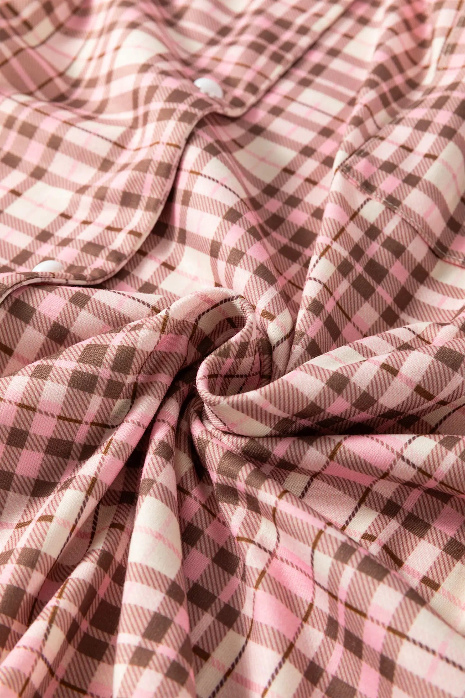 A close-up of a plaid fabric with a soft, draped swirl, showing a pattern of pink, brown, and off-white.