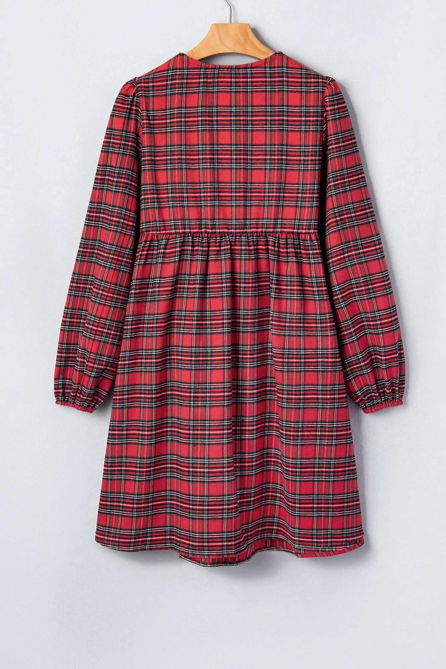 A red and black plaid long-sleeve dress with a gathered waist, hanging on a wooden hanger against a light gray background.