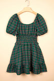A green plaid mini dress with puff sleeves and a smocked waist, hanging on a wooden hanger against a solid beige background.