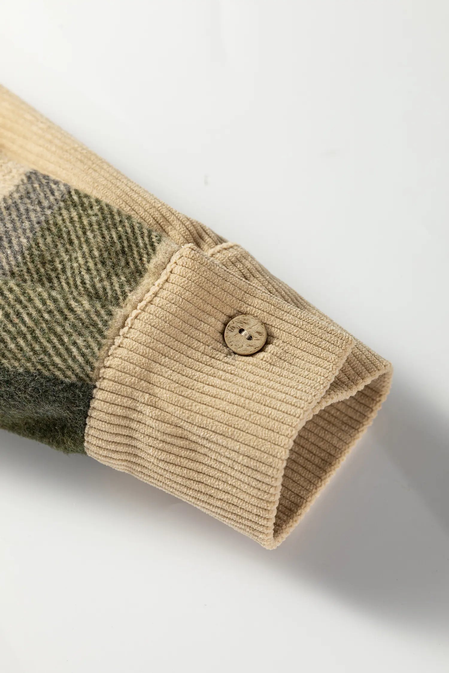 Close-up of a beige ribbed knit cuff with a single wooden button, attached to a plaid fabric sleeve in beige and olive green, on a white background.