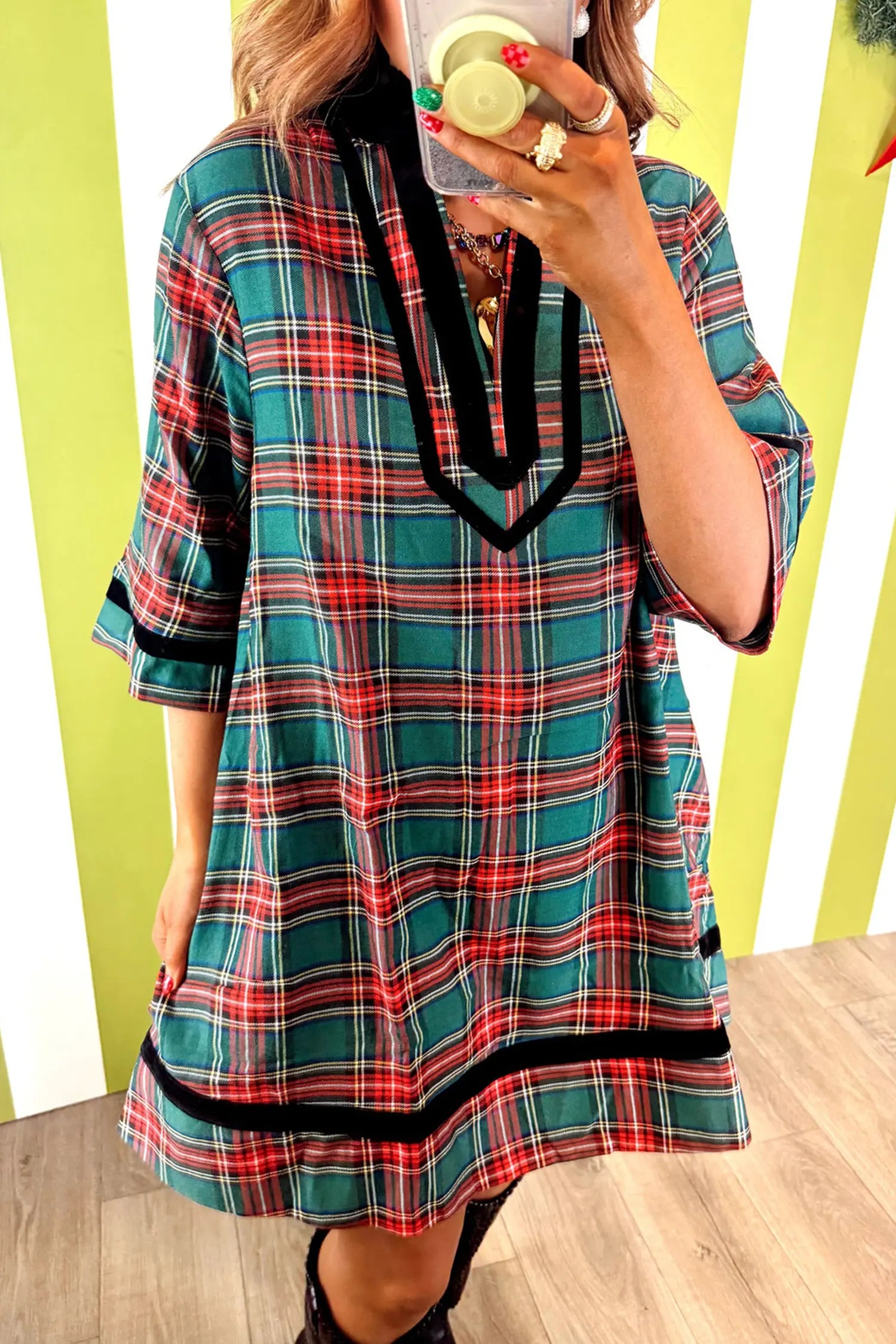 A woman takes a mirror selfie wearing a loose-fitting plaid tunic dress with 3/4 sleeves, featuring a red, green, and blue tartan pattern with black trim.