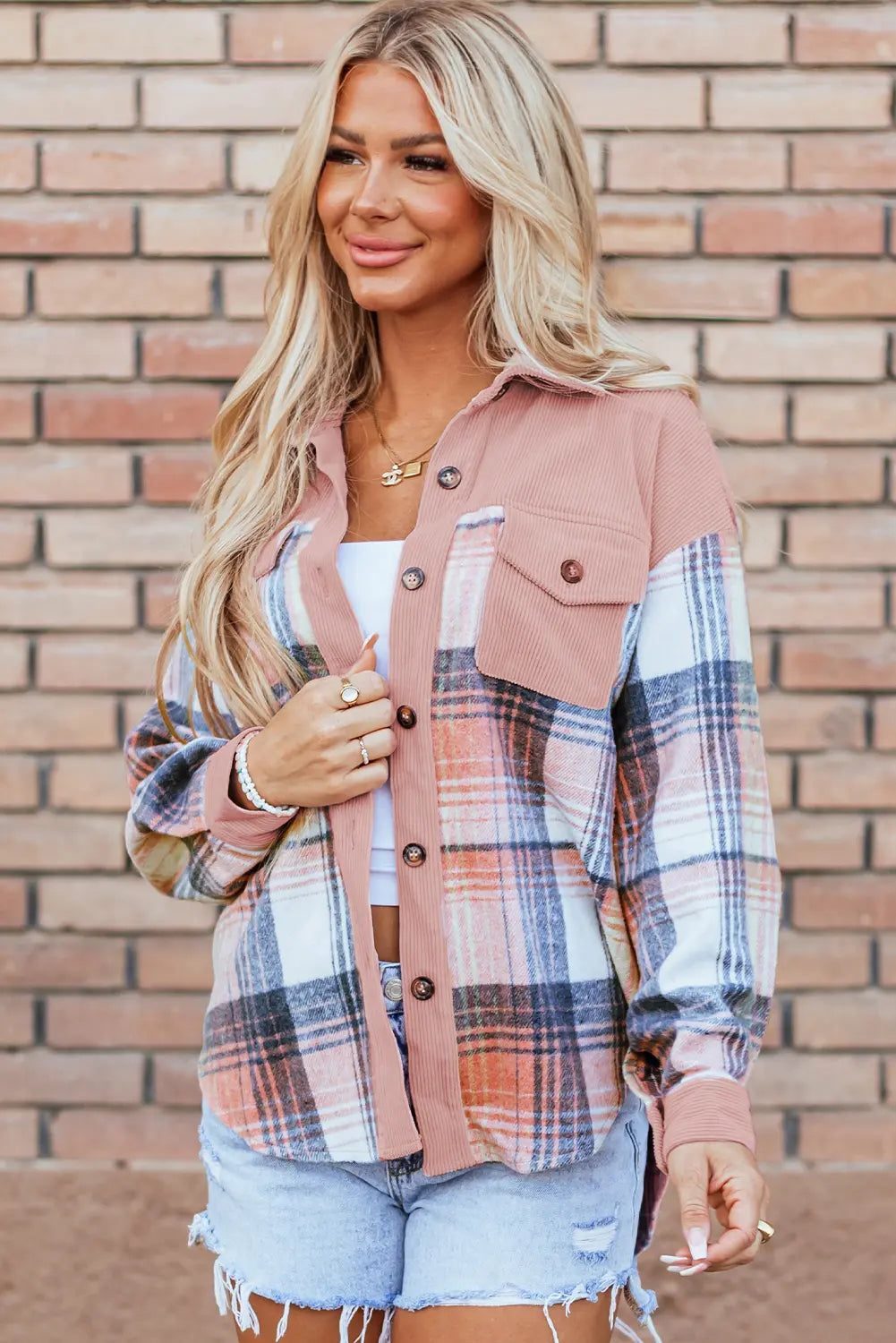Woman wearing a plaid shirt over a pink jacket with a brick wall background